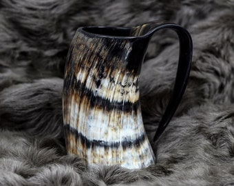 May include: A brown and black drinking horn with a handle. The horn has a natural, striped pattern.
