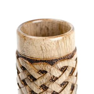 May include: A wooden cup with a carved Celtic knot design. The cup is made of light brown wood with dark brown accents.