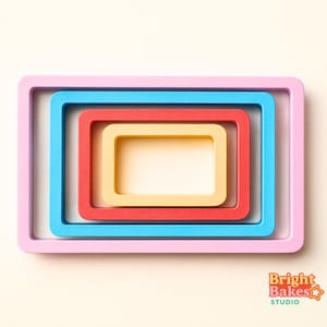 May include: A nested set of rectangular baking molds in pastel colors: pink, blue, red, and yellow. The molds are arranged concentrically, with the smallest yellow mold at the center. The image includes the text "Bright Bakes Studio" in the lower right corner.