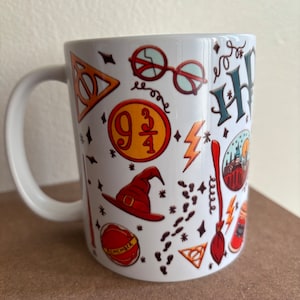 Könnte beinhalten: Weiße Keramiktasse mit einem Harry-Potter-Motiv. Die Tasse zeigt verschiedene Harry-Potter-Symbole und -Charaktere, darunter das Hogwarts-Wappen, einen Blitz, einen Besen, einen Hut und die Zahl 9 3/4. Die Tasse trägt auch die Worte "Remember" und "Always".