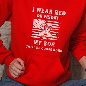 May include: Red hoodie with a white graphic that says "I wear red on Friday for my son until he comes home". The graphic also includes a stylized American flag with a pair of boots.