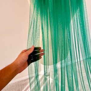May include: A sheer green fabric with a soft, flowing texture. The fabric is draped over a white mannequin and appears to be lightweight and delicate.