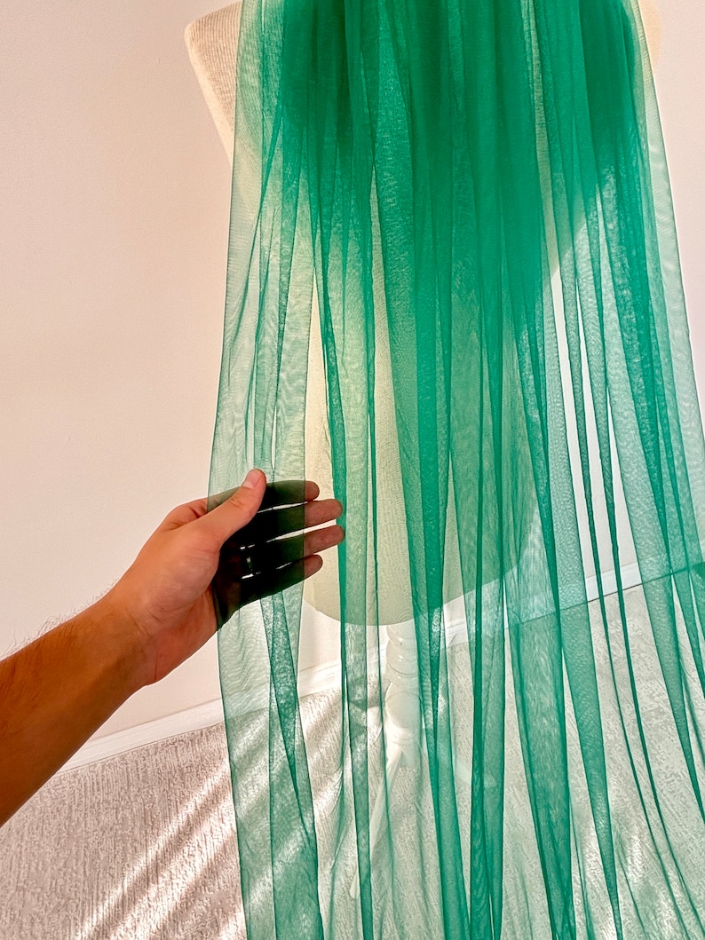May include: A sheer green fabric with a soft, flowing texture. The fabric is draped over a white mannequin and appears to be lightweight and delicate.
