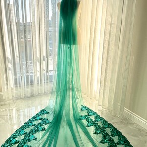 May include: A long, green tulle wedding veil with a sequined border. The veil is draped over a mannequin and is displayed against a white background.