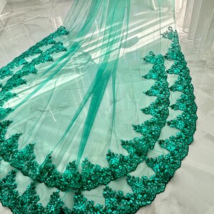 May include: A teal tulle fabric with a double layer of emerald green sequined lace trim.