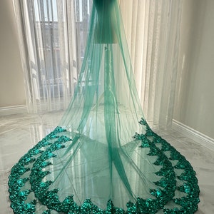 May include: A long, emerald green tulle wedding veil with a double layer of sequined lace trim. The veil is draped over a mannequin and has a cathedral length.