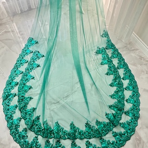 May include: A green tulle wedding veil with a double layer of emerald green lace trim. The lace trim features a floral design with sequins.