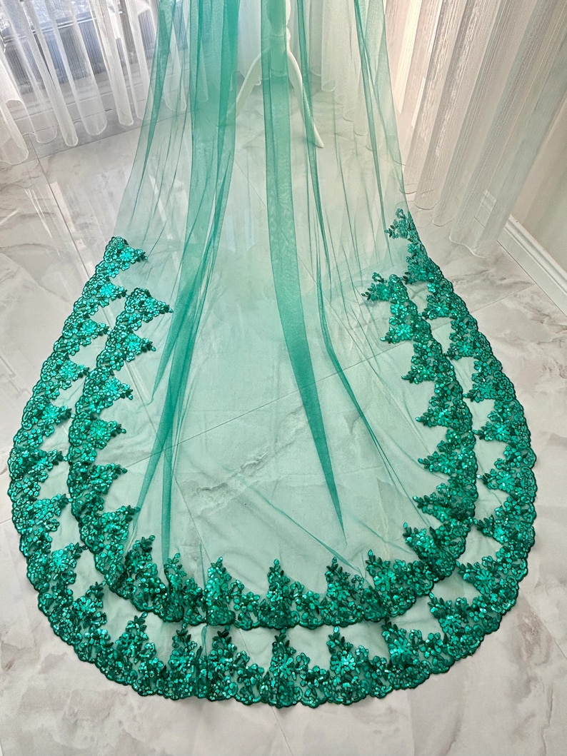 May include: A green tulle wedding veil with a double layer of emerald green lace trim. The lace trim features a floral design with sequins.
