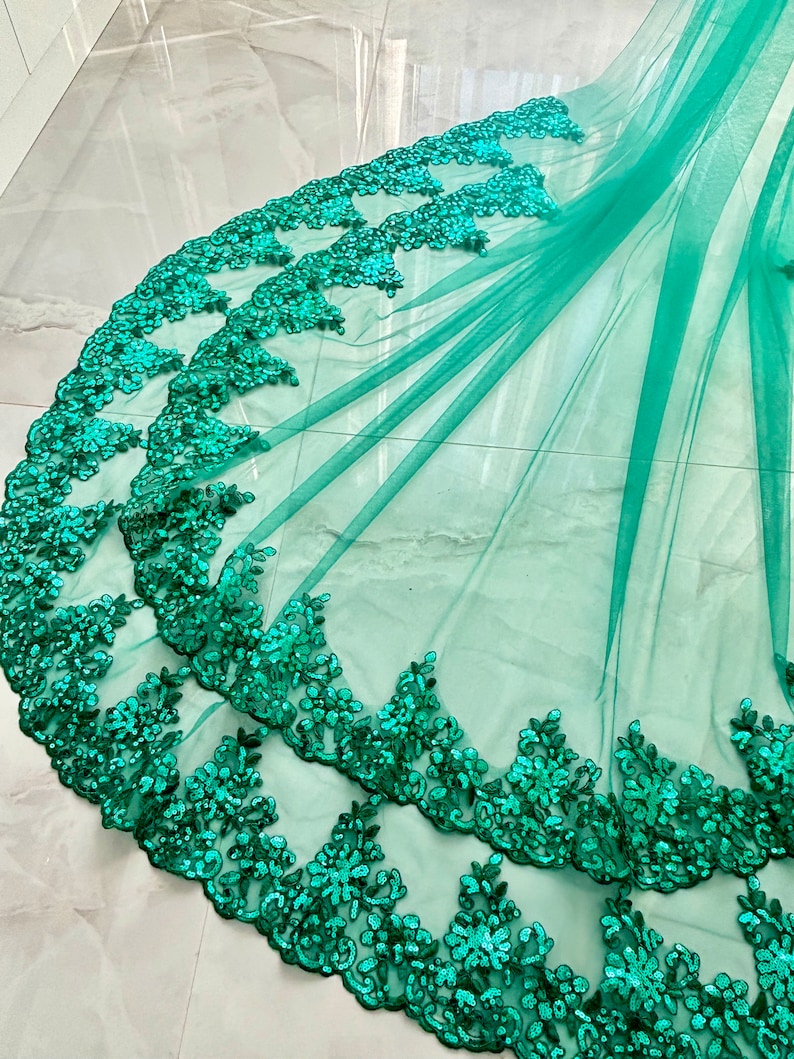 May include: Emerald green tulle fabric with a double layer of sequined lace trim. The lace trim features a floral design.