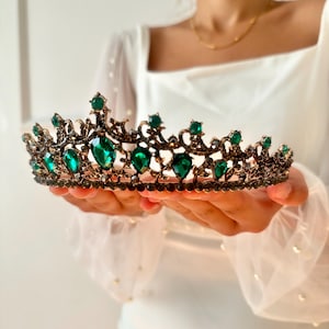 May include: A gold crown with emerald green gemstones. The crown has a delicate, ornate design.