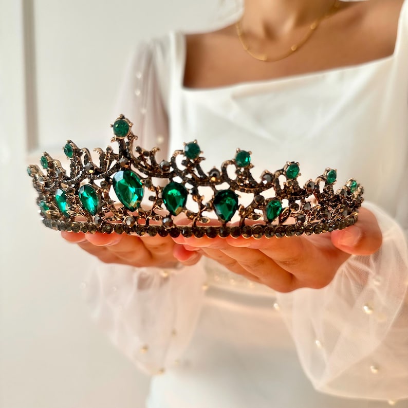 May include: A gold crown with emerald green gemstones. The crown has a delicate, ornate design.