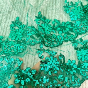 May include: Emerald green sequined lace fabric with a floral design. The lace is delicate and has a soft, flowing texture.