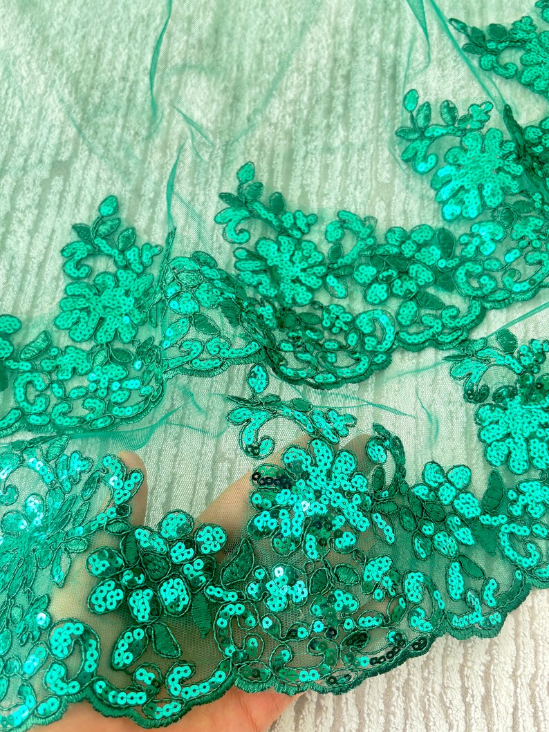 May include: Emerald green sequined lace fabric with a floral design. The lace is delicate and has a soft, flowing texture.