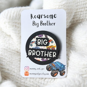 May include: A white card with the text "Roarsome Big Brother" and a black circular badge that says "Big Brother". The badge has a monster truck design. The card also includes social media information.