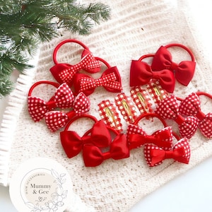 May include: A set of red and white gingham hair bows and red satin hair bows. The bows are arranged on a white crocheted surface. The image includes the text "Hair Accessories Mummy & Gee".