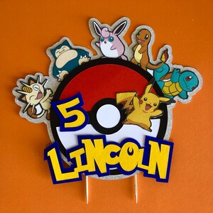May include: A red and white Pokeball cake topper with a silver glitter background. The topper features the number 5, the name Lincoln, and various Pokemon characters including Pikachu, Squirtle, and Meowth.