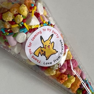 May include: A clear plastic cone filled with colourful sprinkles, cereal, and marshmallows. A round sticker with a cartoon Pikachu and the text "Thank you for coming to my party Love from Grayson" is attached to the cone.