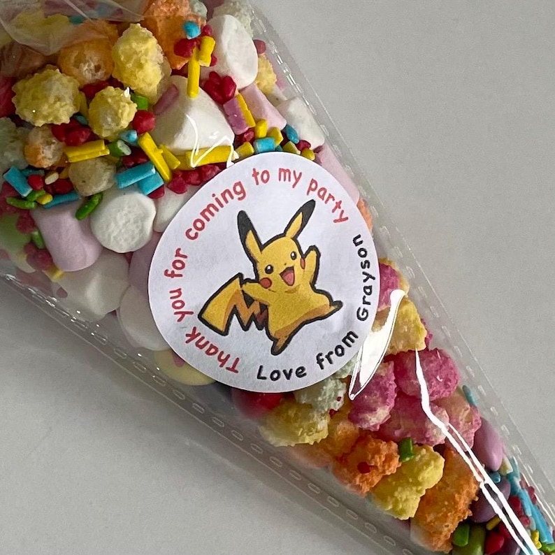 May include: A clear plastic cone filled with colourful sprinkles, cereal, and marshmallows. A round sticker with a cartoon Pikachu and the text "Thank you for coming to my party Love from Grayson" is attached to the cone.