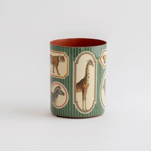 May include: A cylindrical container featuring a dark green vertical striped background with various animal illustrations enclosed in decorative frames, including a giraffe, a tiger, and a zebra, with a solid reddish-orange interior lining.