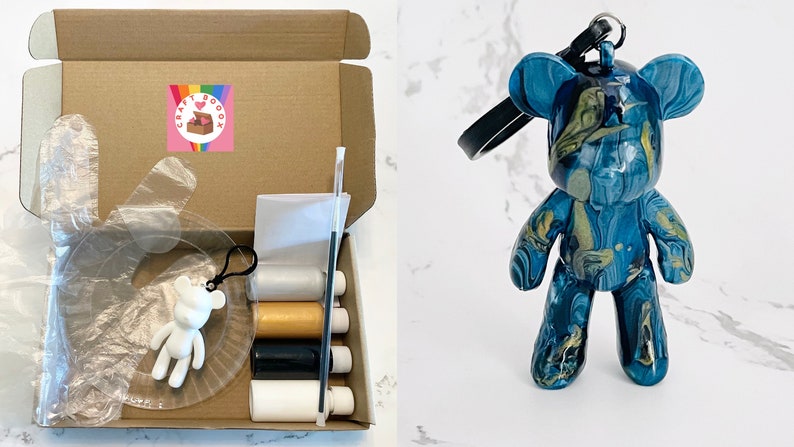 Pode incluir: Um kit de caixa de artesanato com um adesivo com o logotipo do arco-&iacute;ris, contendo uma luva de pl&aacute;stico transparente, um chaveiro em forma de urso branco e v&aacute;rios materiais de artesanato. Um chaveiro em forma de urso azul e dourado com uma al&ccedil;a preta tamb&eacute;m &eacute; mostrado.