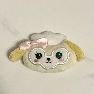 May include: A plush toy of a dog wearing a white hat with a pink bow. The dog has green eyes, a pink nose, and a white and gray face.