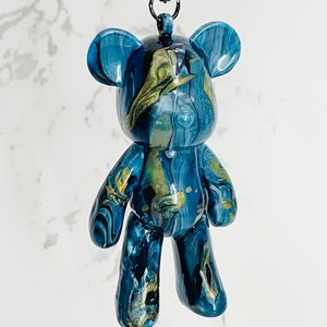 Pode incluir: Estatueta de urso em resina marmoreada azul e dourada com um cord&atilde;o preto. O urso tem um acabamento brilhante e um padr&atilde;o &uacute;nico em espiral. A estatueta &eacute; um item decorativo.