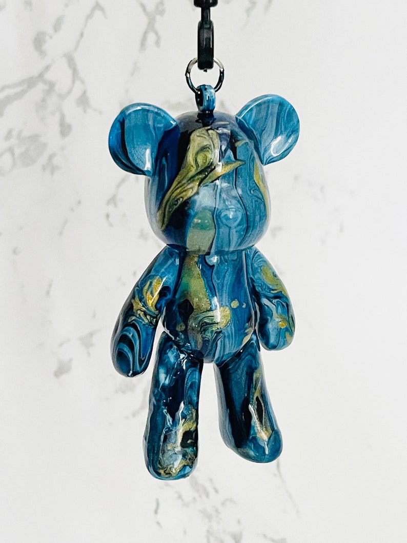 Pode incluir: Estatueta de urso em resina marmoreada azul e dourada com um cord&atilde;o preto. O urso tem um acabamento brilhante e um padr&atilde;o &uacute;nico em espiral. A estatueta &eacute; um item decorativo.