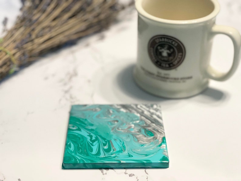 Peut inclure: Un dessous de verre carr&eacute; avec un motif marbr&eacute; turquoise, argent et blanc. Le dessous de verre est fait d'un mat&eacute;riau lisse et dur et a une finition brillante.