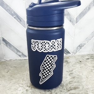 Pu&ograve; includere: Una bottiglia d'acqua blu con un adesivo a forma di fulmine a scacchi bianco e nero e il nome "JUDAH" in lettere a scacchi bianco e nero.
