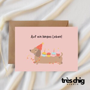 Postkarte "Auf ein langes Leben Dackel“ von Très Chig Studio, Weihnachtsgeschenk, Winter, Pullover, Hund, Lichterkette, lustig, Haustier
