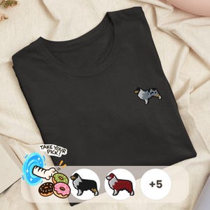 May include: A black t-shirt featuring a small embroidered blue merle Australian Shepherd dog on the chest. Below, a graphic shows a hand reaching into a blue portal with donuts and two additional dog embroidery options, plus a plus five icon.