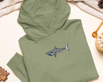 May include: A sage green hooded sweatshirt featuring an embroidered graphic of a grey shark with a small blue object in its mouth. The hoodie has long sleeves, a front kangaroo pocket, and a drawstring-free hood with a structured neckline.