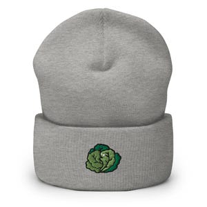 May include: A gray beanie with a green embroidered cabbage design on the front. The beanie is made of a soft, knitted material and has a folded cuff. This hat is a stylish accessory for cooler weather.