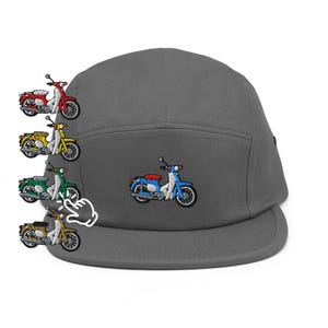 Könnte beinhalten: Graue Fünf-Panel-Kappe mit einem gestickten blau-rot-weißen Motorroller-Design. Zusätzliche gestickte Motorroller-Designs in Rot, Gelb, Grün und Braun sind auf der linken Seite der Kappe abgebildet.