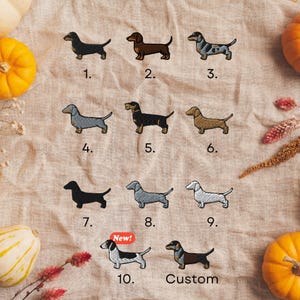 a collection of nine dachshund dog illustrations, each with a unique color and style, arranged on a beige background. The illustrations are accompanied by the numbers 1 through 9, which may indicate a selection or a numbering system for the images. In the bottom right corner, there is a red "New!" sign, suggesting that the image may be a new or recently added collection. The text "Custom" is also present, indicating that the illustrations are customizable.