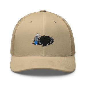 May include: Tan trucker hat with a mesh back and a curved brim. The front panel features an embroidered design of a person looking into a black hole. The person is wearing a gray jacket and blue jeans.