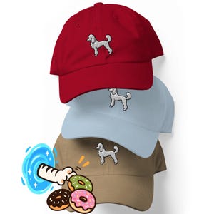 Peut inclure: Une pile de trois casquettes de baseball rouge, bleu clair et beige, chacune ornée d'une silhouette de caniche blanche brodée sur le panneau avant. Un graphique de patte de chat traversant un portail bleu vers trois beignets est visible.
