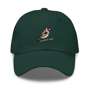 Puede incluir: Una gorra de béisbol de color verde bosque oscuro con un parche bordado de un jilguero posado en una rama marrón. El ave tiene la cara roja, la cabeza negra y blanca y marcas amarillas en las alas. La gorra tiene una visera curva y estructurada.