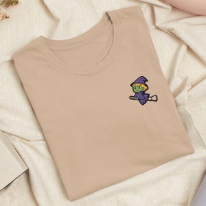 Witch Flying on Broomstick Embroidered T-Shirt with Comfortable Stretch - Soft, Lightweight, Variety of Colors - Spooky Halloween Sorceress