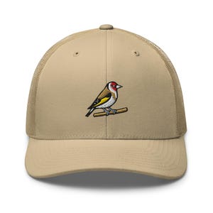 Op de afbeelding: Een beige truckerpet met een mesh achterkant en een stevig voorpaneel. In het midden staat een geborduurde afbeelding van een putter met een rode kop, zwart-witte markeringen en gele vleugelvlekken, zittend op een bruine tak.