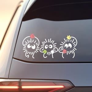 May include: Three white cartoon characters with black eyes and spiky hair are on a black car window. Each character has a small star above their head in different colors: red, green, and yellow.