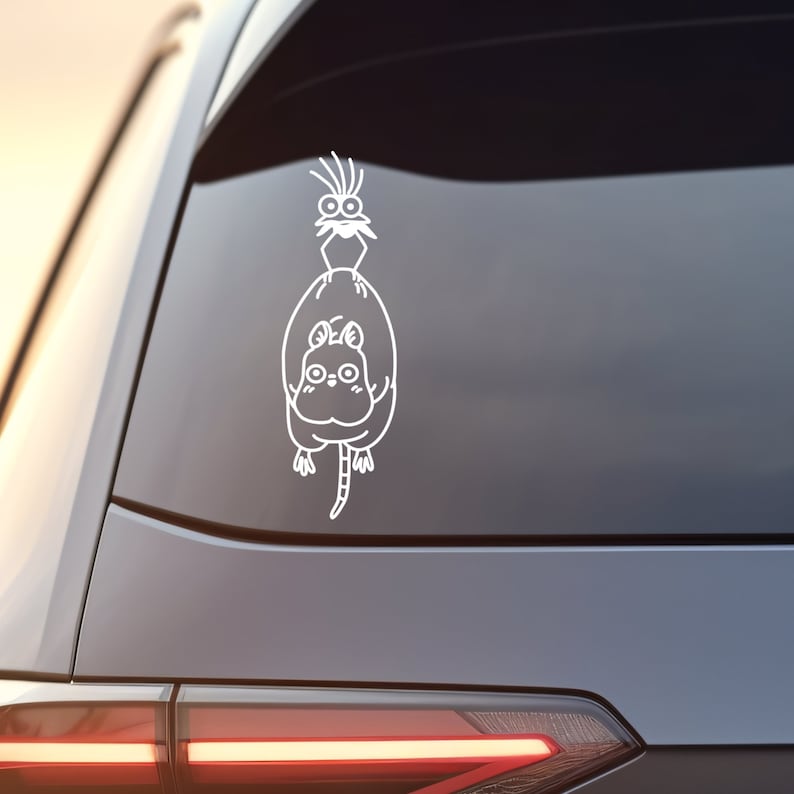May include: White vinyl sticker of a cartoon cat with a bird on its back. The cat is sitting up and the bird is perched on its back. The sticker is on the back window of a car.