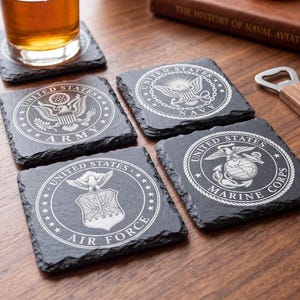 Puede incluir: Cuatro posavasos cuadrados de pizarra negra con emblemas grabados con l&aacute;ser en blanco del Ej&eacute;rcito, la Armada, la Fuerza A&eacute;rea y el Cuerpo de Marines de los Estados Unidos. Cada posavasos tiene un borde natural y rugoso.