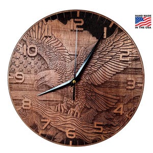 May include: A wooden clock with a carved image of an eagle with its wings spread. The clock face has Roman numerals and is surrounded by a wood grain pattern. The clock is hand-made in the USA.