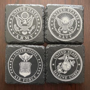 Puede incluir: Cuatro posavasos cuadrados de pizarra negra con emblemas grabados con l&aacute;ser en blanco de las ramas militares de EE. UU. Los dise&ntilde;os incluyen los sellos del Army, Navy, Air Force y Marine Corps, centrados dentro de un borde circular.