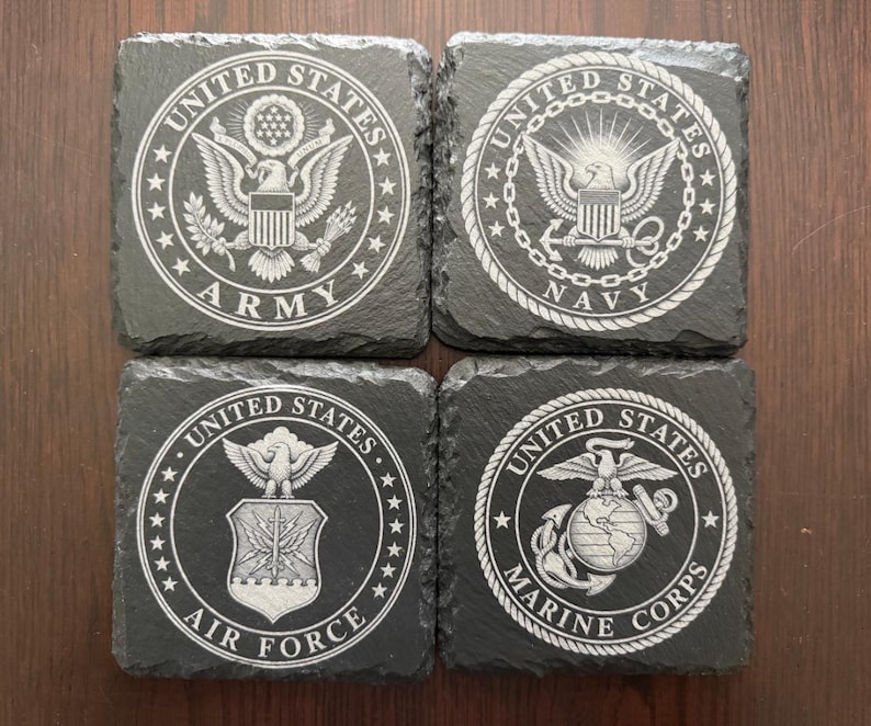 Puede incluir: Cuatro posavasos cuadrados de pizarra negra con emblemas grabados con l&aacute;ser en blanco de las ramas militares de EE. UU. Los dise&ntilde;os incluyen los sellos del Army, Navy, Air Force y Marine Corps, centrados dentro de un borde circular.