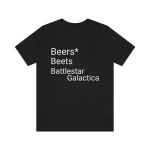 Puede incluir: Camiseta negra con texto blanco: "Beers* Beets Battlestar Galactica". La camiseta, de cuello redondo, está hecha de un tejido suave.