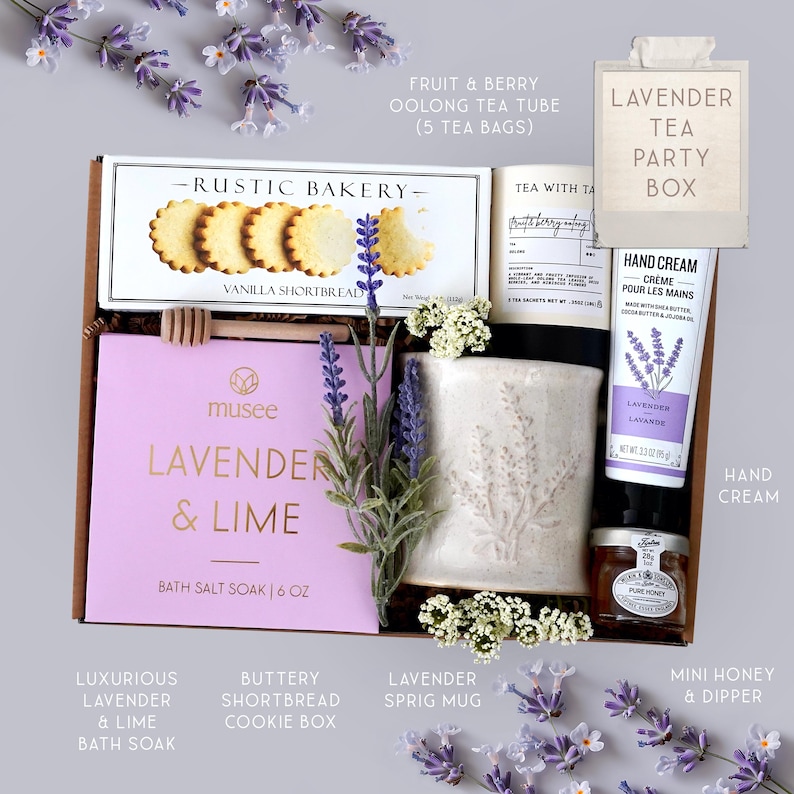 K&ouml;nnte beinhalten: Eine Geschenkbox mit Lavendel-Thema. Enth&auml;lt ein Lavendel- und Limetten-Badesalz, Vanille-Shortbread-Kekse, eine Tasse mit Zweig-Motiv, Handcreme, Mini-Honig und Tee. Die Box ist mit Lavendelzweigen und dem Text "Lavender Tea Party Box" verziert.