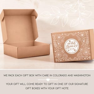May include: Two light brown cardboard gift boxes. One box is open with an empty interior. The other box is closed and features a white circular logo with the text "wild flower pop" surrounded by intricate white line drawings of various flowers.