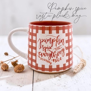 Puede incluir: Una taza de cer&aacute;mica con un patr&oacute;n de cuadros blancos y naranjas y un acabado moteado. El frente presenta el texto "pumpkin spice AND everything nice" en letra cursiva naranja. El interior de la taza es de color naranja s&oacute;lido.